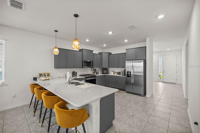 kitchen featuring light tile patterned flooring, a kitchen bar, decorative light fixtures, appliances with stainless steel finishes, and kitchen peninsula