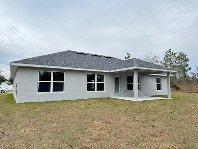 back of house with a patio area, a lawn, and roof with shingles