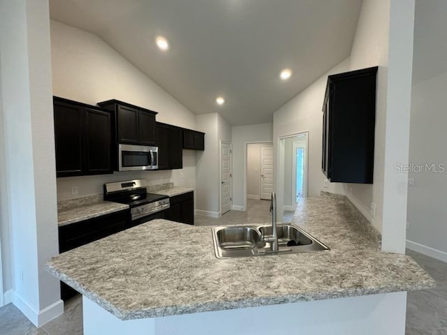 kitchen with light countertops, appliances with stainless steel finishes, a sink, dark cabinetry, and a peninsula