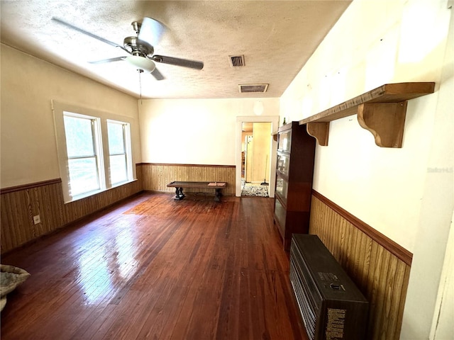 interior space with wood walls, ceiling fan, dark wood-type flooring, and a textured ceiling