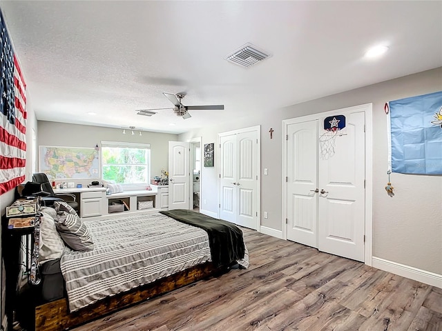 bedroom featuring a textured ceiling, wood-type flooring, two closets, and ceiling fan