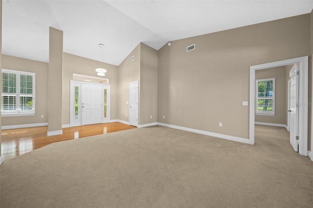 unfurnished living room with high vaulted ceiling and light colored carpet