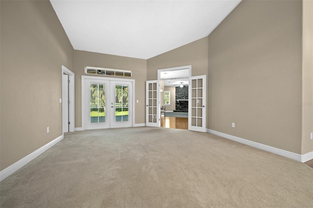 unfurnished living room with light carpet, high vaulted ceiling, and french doors