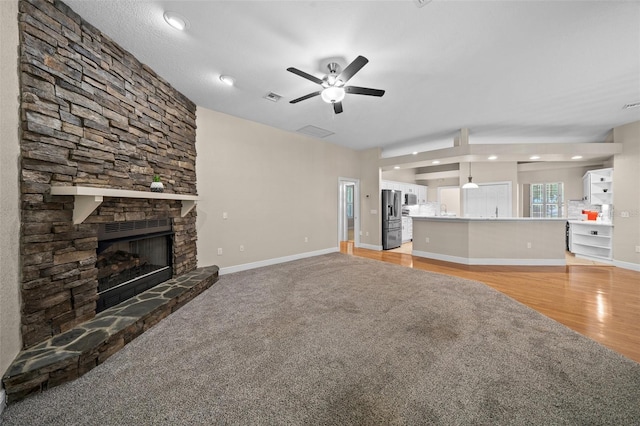 unfurnished living room featuring ceiling fan, a stone fireplace, and light hardwood / wood-style flooring