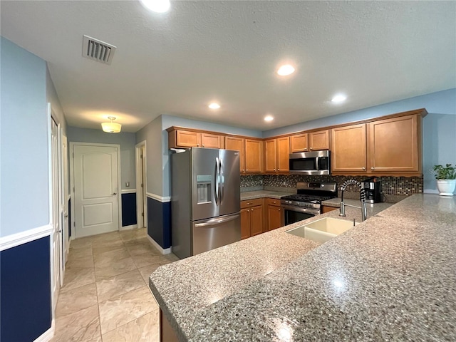 kitchen featuring tasteful backsplash, stainless steel appliances, stone counters, light tile patterned floors, and kitchen peninsula