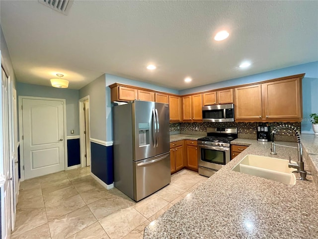 kitchen with light tile patterned flooring, appliances with stainless steel finishes, light stone countertops, sink, and decorative backsplash