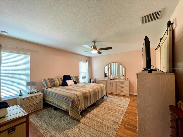 bedroom with ceiling fan, a barn door, multiple windows, and light hardwood / wood-style floors