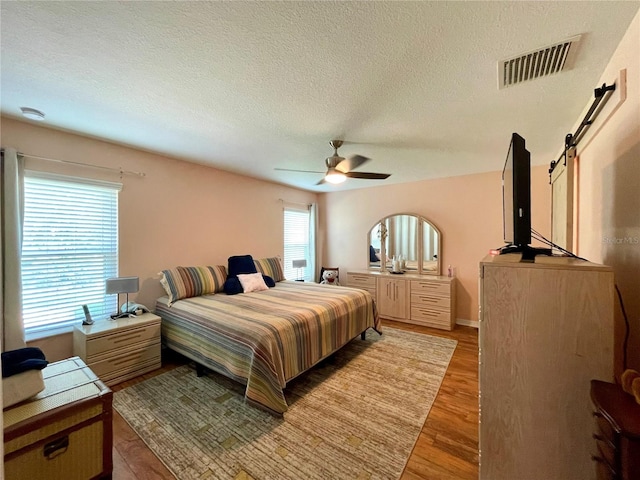 bedroom with ceiling fan, a barn door, hardwood / wood-style flooring, and a textured ceiling