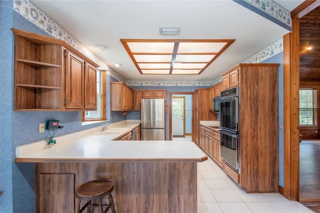 kitchen featuring black appliances, a textured ceiling, light tile patterned floors, kitchen peninsula, and a breakfast bar