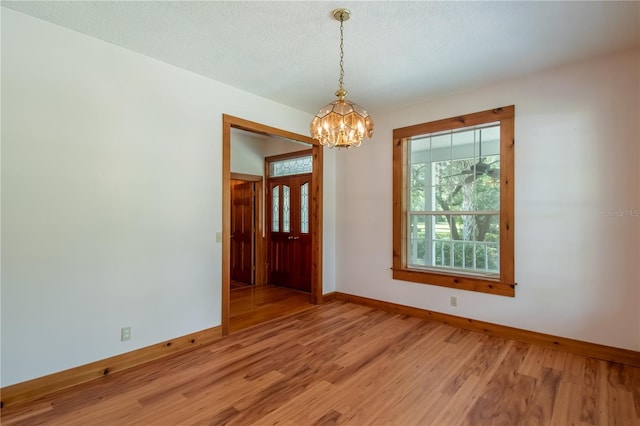 empty room with an inviting chandelier, a textured ceiling, baseboards, and light wood-style floors