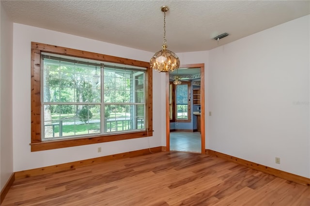 empty room featuring light wood-type flooring, a notable chandelier, and a textured ceiling