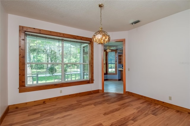 unfurnished room with visible vents, baseboards, a chandelier, light wood-style flooring, and a textured ceiling