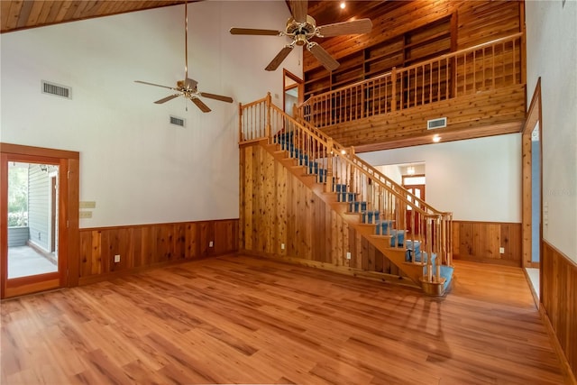 unfurnished living room featuring wood walls, high vaulted ceiling, wood-type flooring, ceiling fan, and wood ceiling