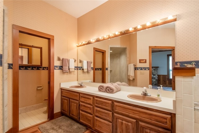 bathroom with wallpapered walls, double vanity, toilet, and a sink