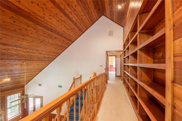 hallway with visible vents, light colored carpet, wood ceiling, an upstairs landing, and high vaulted ceiling