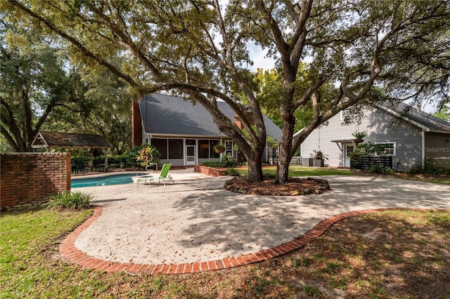 rear view of property featuring an outdoor pool, a patio area, and a sunroom