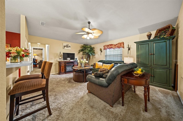 living area featuring carpet floors, a glass covered fireplace, visible vents, and a ceiling fan