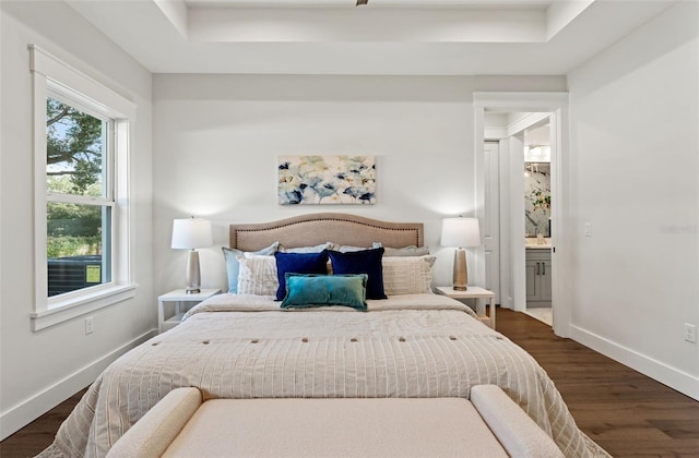 bedroom with connected bathroom, a tray ceiling, and dark wood-type flooring