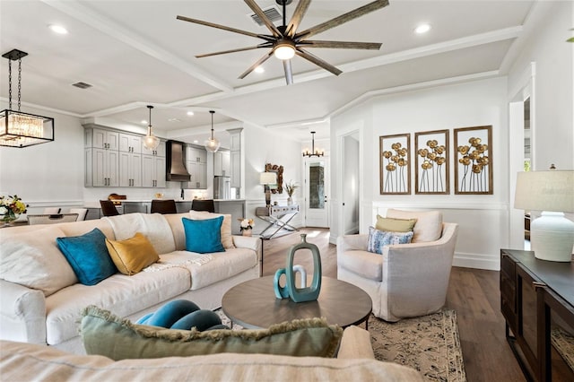 living room with beamed ceiling, ceiling fan with notable chandelier, ornamental molding, and dark wood-type flooring