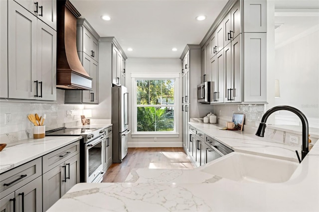 kitchen with appliances with stainless steel finishes, light stone counters, custom range hood, and sink