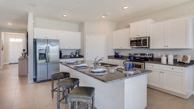 kitchen with dark stone counters, a kitchen island with sink, light tile patterned floors, stainless steel appliances, and sink