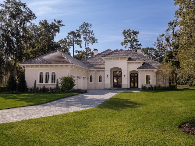 view of front of home with stucco siding, decorative driveway, french doors, a front yard, and a chimney