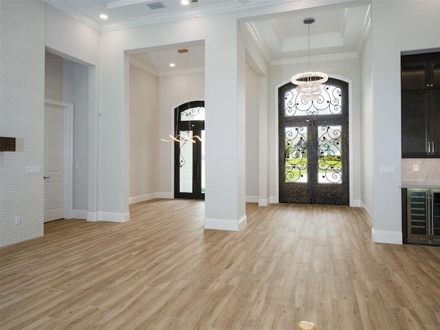 foyer entrance featuring light hardwood / wood-style floors, a raised ceiling, ornamental molding, and french doors