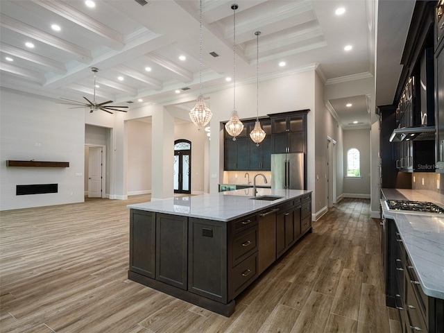 kitchen featuring light wood finished floors, tasteful backsplash, beamed ceiling, appliances with stainless steel finishes, and a sink