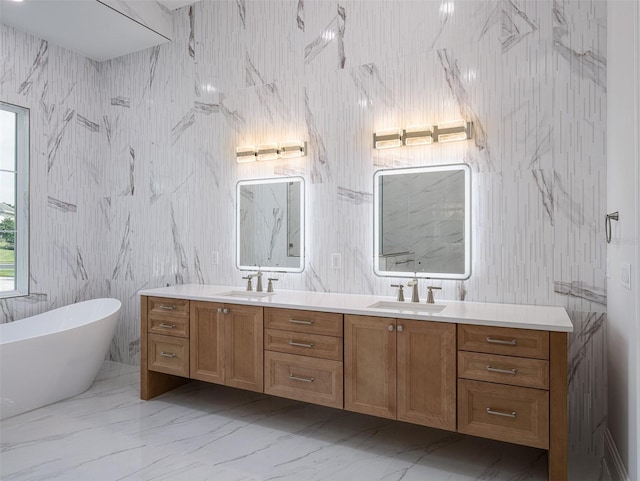 bathroom featuring a sink, a freestanding bath, marble finish floor, and double vanity
