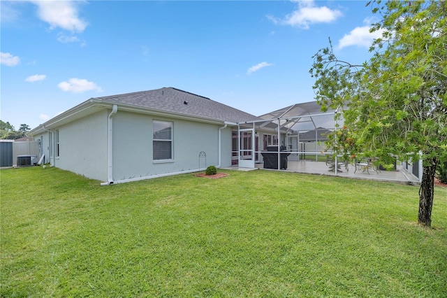 rear view of property with a lawn, glass enclosure, and central AC