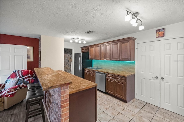 kitchen featuring a textured ceiling, a breakfast bar area, stainless steel appliances, and backsplash