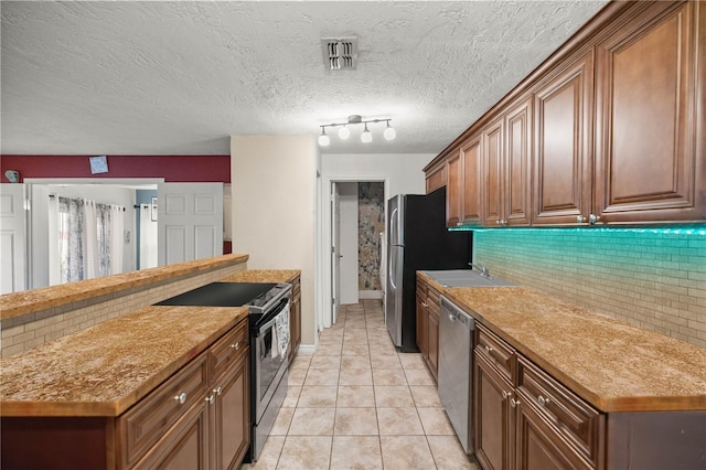 kitchen featuring light tile patterned floors, a textured ceiling, rail lighting, stainless steel appliances, and decorative backsplash