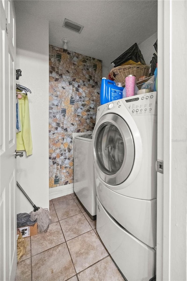 clothes washing area featuring light tile patterned flooring, washing machine and dryer, and a textured ceiling