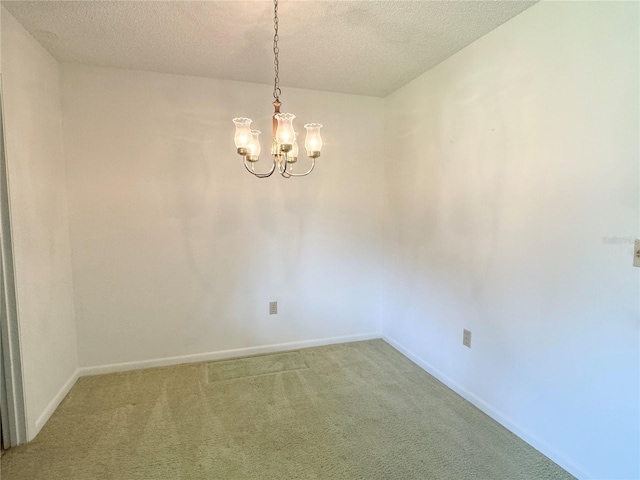 spare room featuring a textured ceiling, carpet flooring, and an inviting chandelier