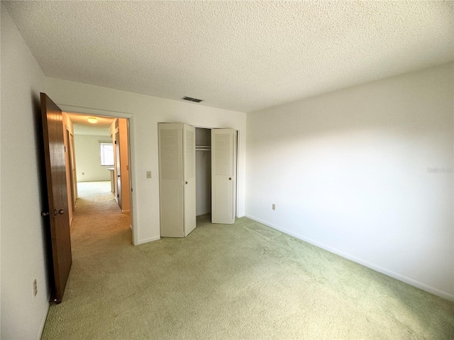 unfurnished bedroom with a closet, a textured ceiling, and light colored carpet