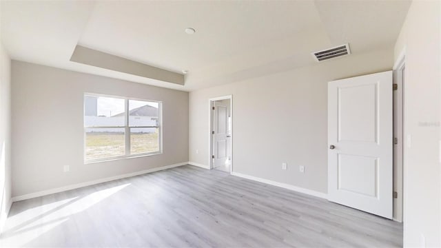 empty room featuring light hardwood / wood-style floors and a tray ceiling