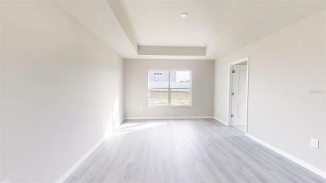 empty room with a raised ceiling and light hardwood / wood-style flooring