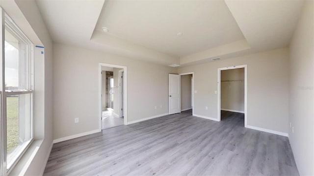 unfurnished bedroom with ensuite bath, light hardwood / wood-style floors, a spacious closet, and a tray ceiling