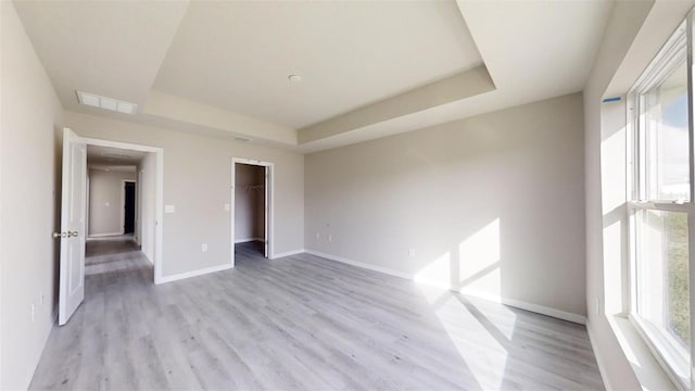 unfurnished bedroom with light wood-type flooring, a closet, a raised ceiling, and a spacious closet