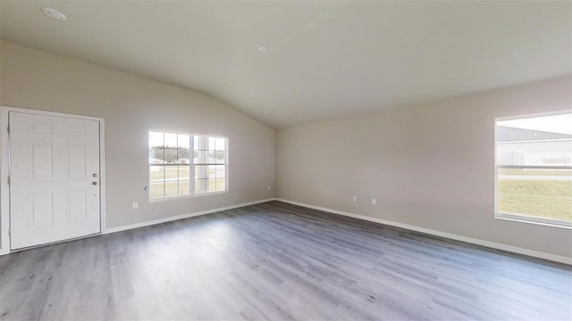 spare room featuring light wood-type flooring and vaulted ceiling