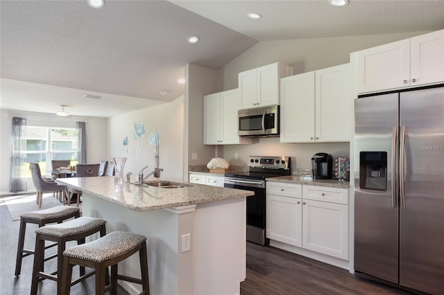 kitchen with appliances with stainless steel finishes, sink, light stone counters, dark hardwood / wood-style flooring, and a breakfast bar