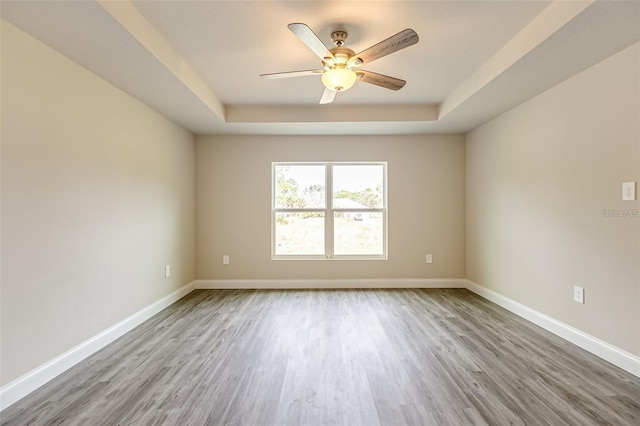 empty room featuring ceiling fan, a raised ceiling, and wood-type flooring