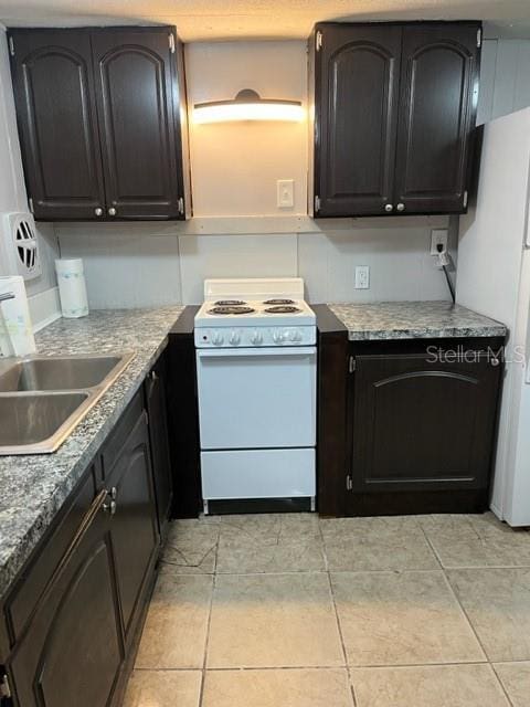 kitchen featuring light tile patterned flooring, dark stone countertops, white appliances, and sink