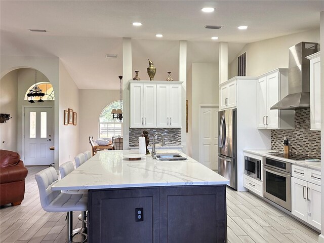 kitchen with sink, wall chimney exhaust hood, an island with sink, a kitchen bar, and stainless steel appliances