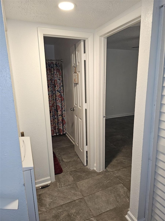 corridor with a textured ceiling and dark tile patterned flooring