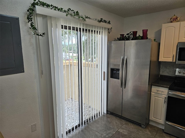 kitchen with tile patterned flooring, a textured ceiling, electric panel, white cabinets, and appliances with stainless steel finishes