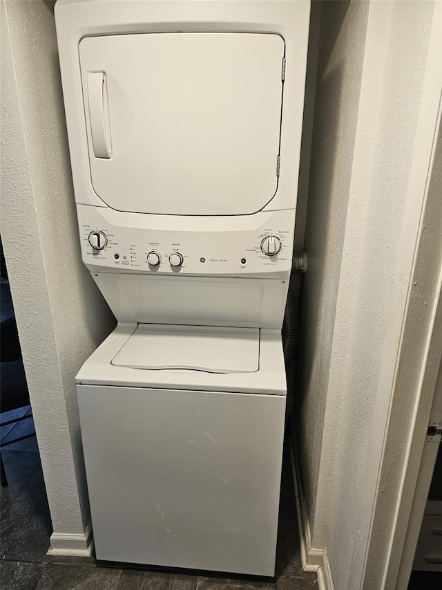 laundry area featuring dark tile patterned flooring and stacked washer / drying machine