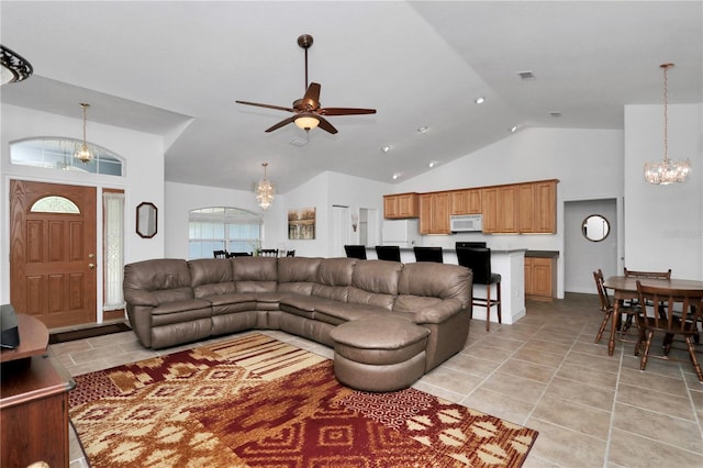 living area with ceiling fan with notable chandelier, high vaulted ceiling, light tile patterned floors, and visible vents