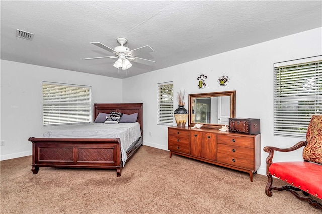 bedroom featuring multiple windows, visible vents, a textured ceiling, and light colored carpet