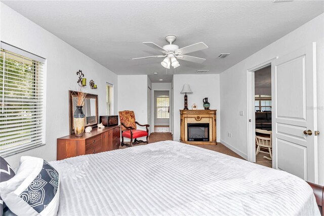 bedroom with a textured ceiling, a fireplace, visible vents, and a ceiling fan